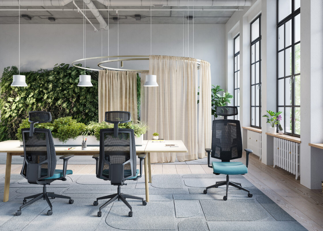 Open-plan office with a curved beige curtain divider, green wall plants, and black ergonomic chairs around light wood desks.",